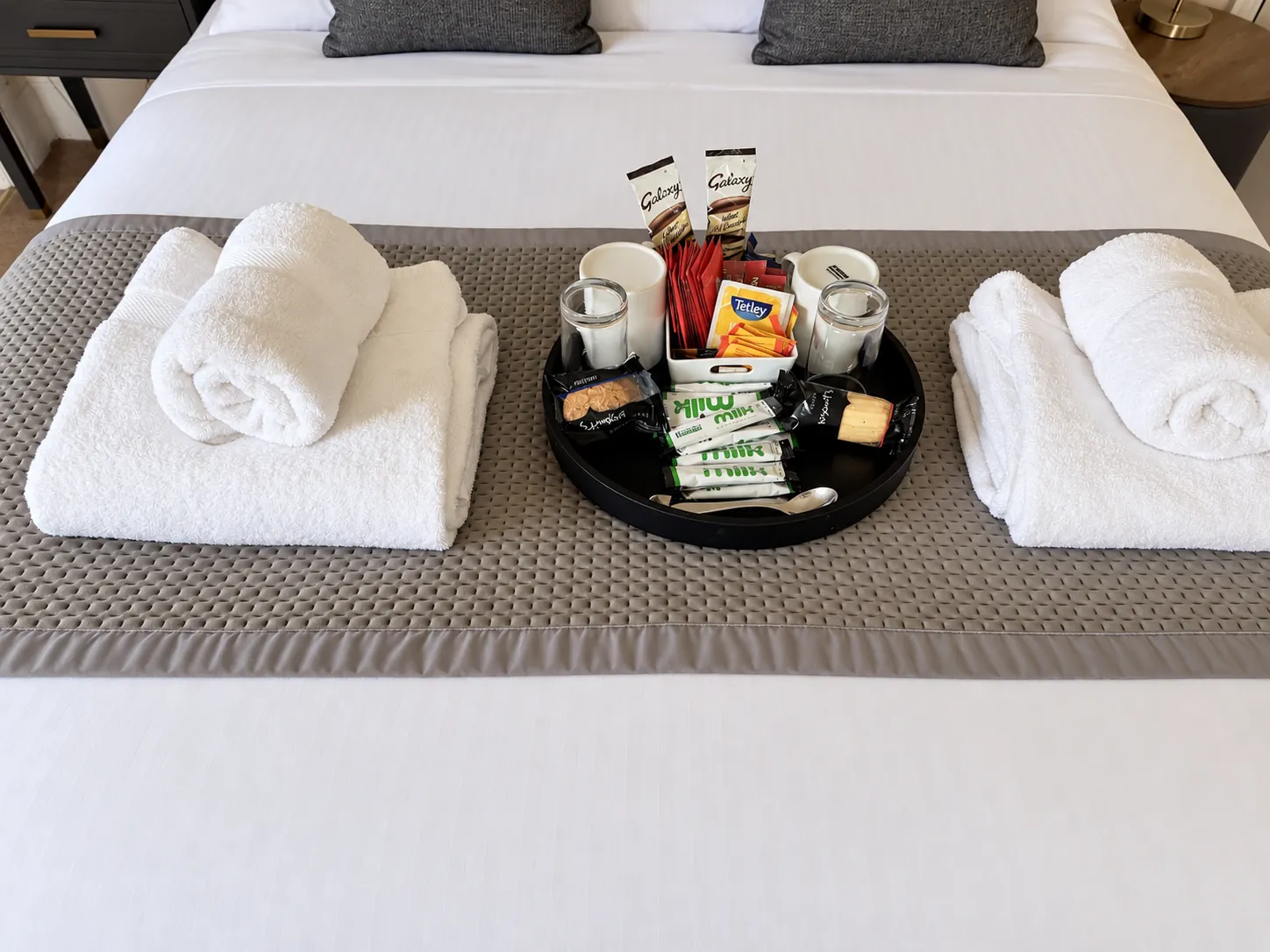 Green Room bed with neatly folded towels and a welcome tray
